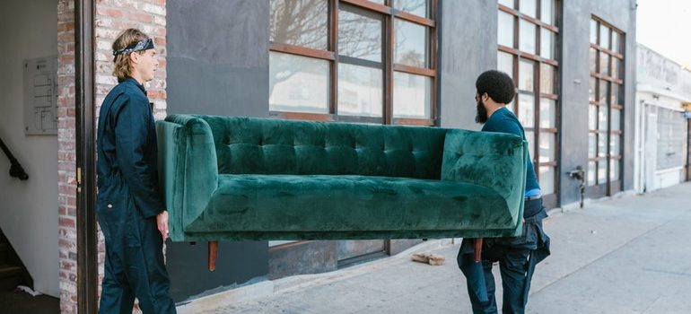 Two man carrying a green sofa. 